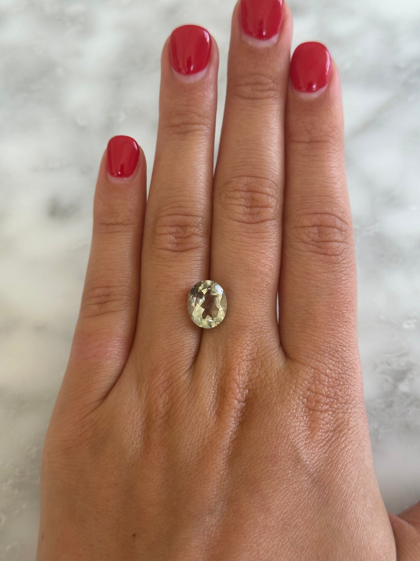 Hand wearing a gold ring with a clear gemstone on a marble background