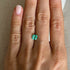 Close-up of a hand with a green emerald gemstone on a neutral background