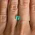 Close-up of a hand with a green emerald gemstone on a neutral background