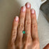Hand with a green gemstone ring on a neutral background
