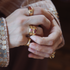 Close-up of hands wearing gold rings with gemstones on a blurred background