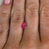 Close-up of a hand with a pink spinel gemstone between the fingers