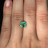 Green emerald gemstone on a finger against a dark background