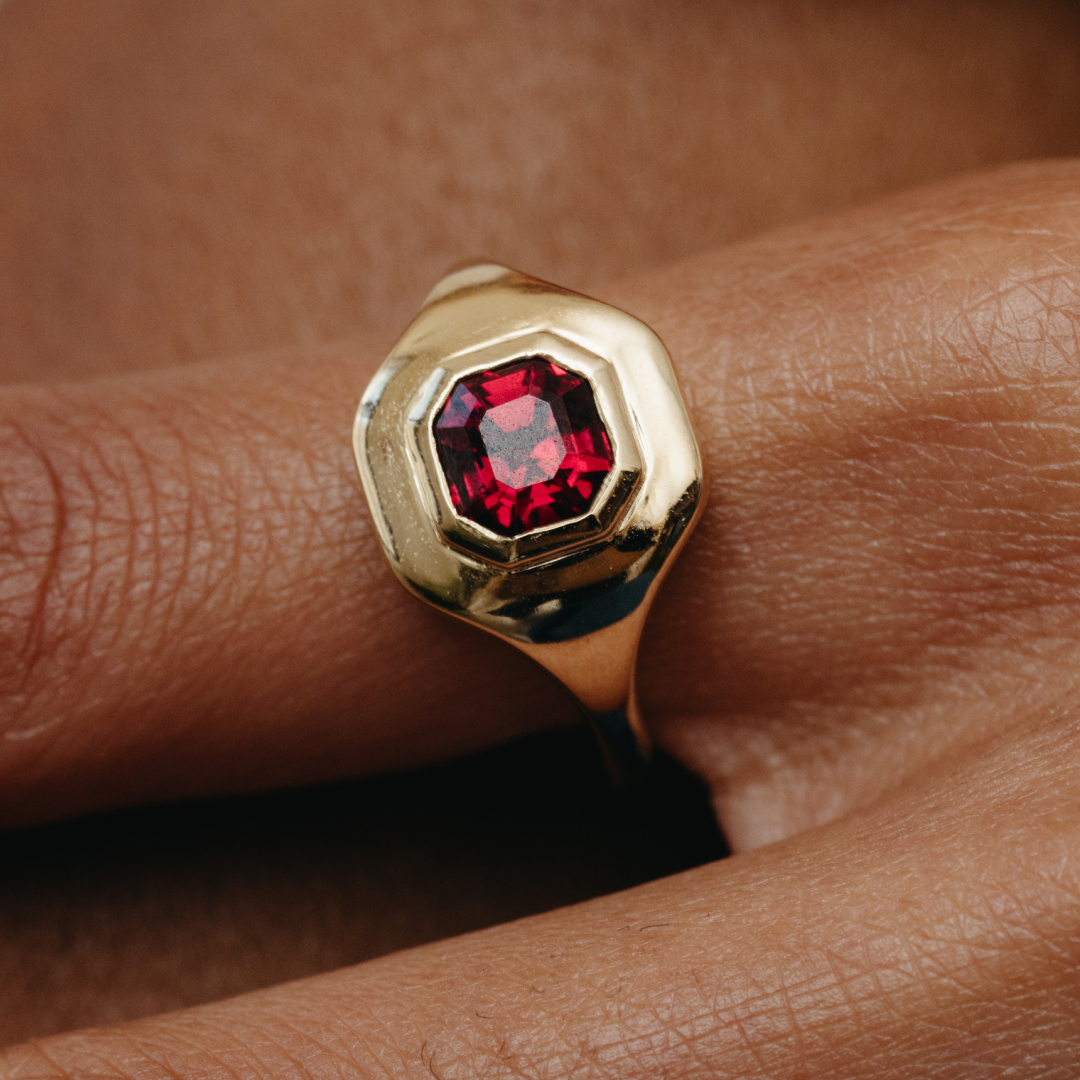Gold ring with a red gemstone on a person's finger