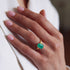 Hand wearing a gold ring with a green gemstone on a blurred background