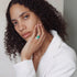 Woman wearing green engagement ring with a white blazer with a neutral background