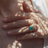 Close-up of a hand wearing two rings with emerald stones on a light background