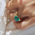 Gold ring with a green gemstone worn on a finger against a neutral background