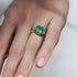 Gold ring with a green emerald gemstone on a hand against a white background
