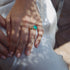 Close-up of a hand wearing a ring with a green gemstone on a white fabric background