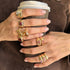 Close-up of hands wearing gold rings with gemstones holding a coffee cup.