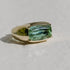 A gold ring with a large mint green tourmaline gemstone set in a rectangular cut on a neutral background