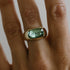 A gold ring with a large mint green tourmaline gemstone set in a rectangular cut on a finger
