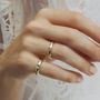 Close-up of a hand wearing two gold rings with small stones on a light background