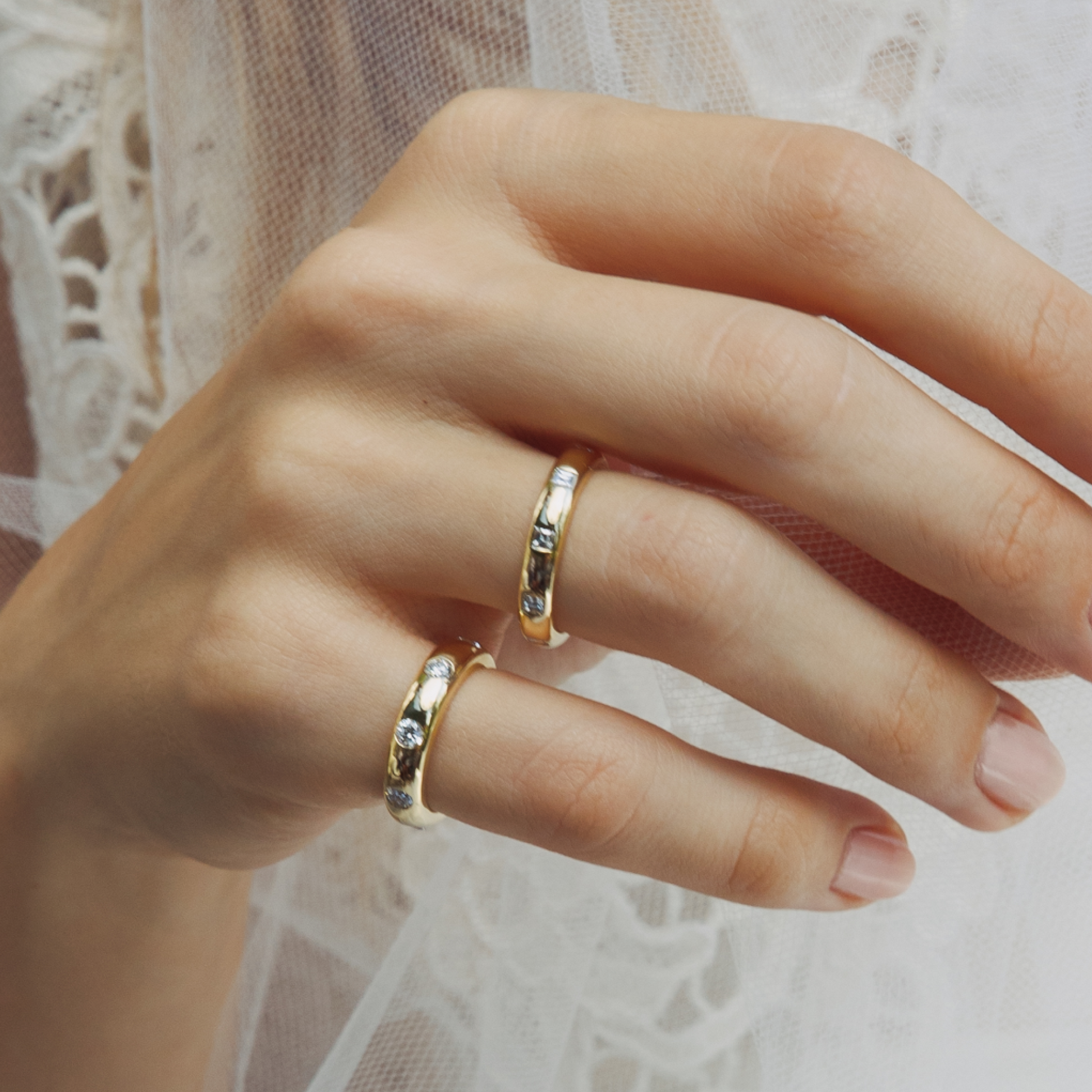 Close-up of a hand wearing two gold rings with small stones on a light background