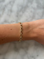 Gold chain bracelet on a wrist against a marble background