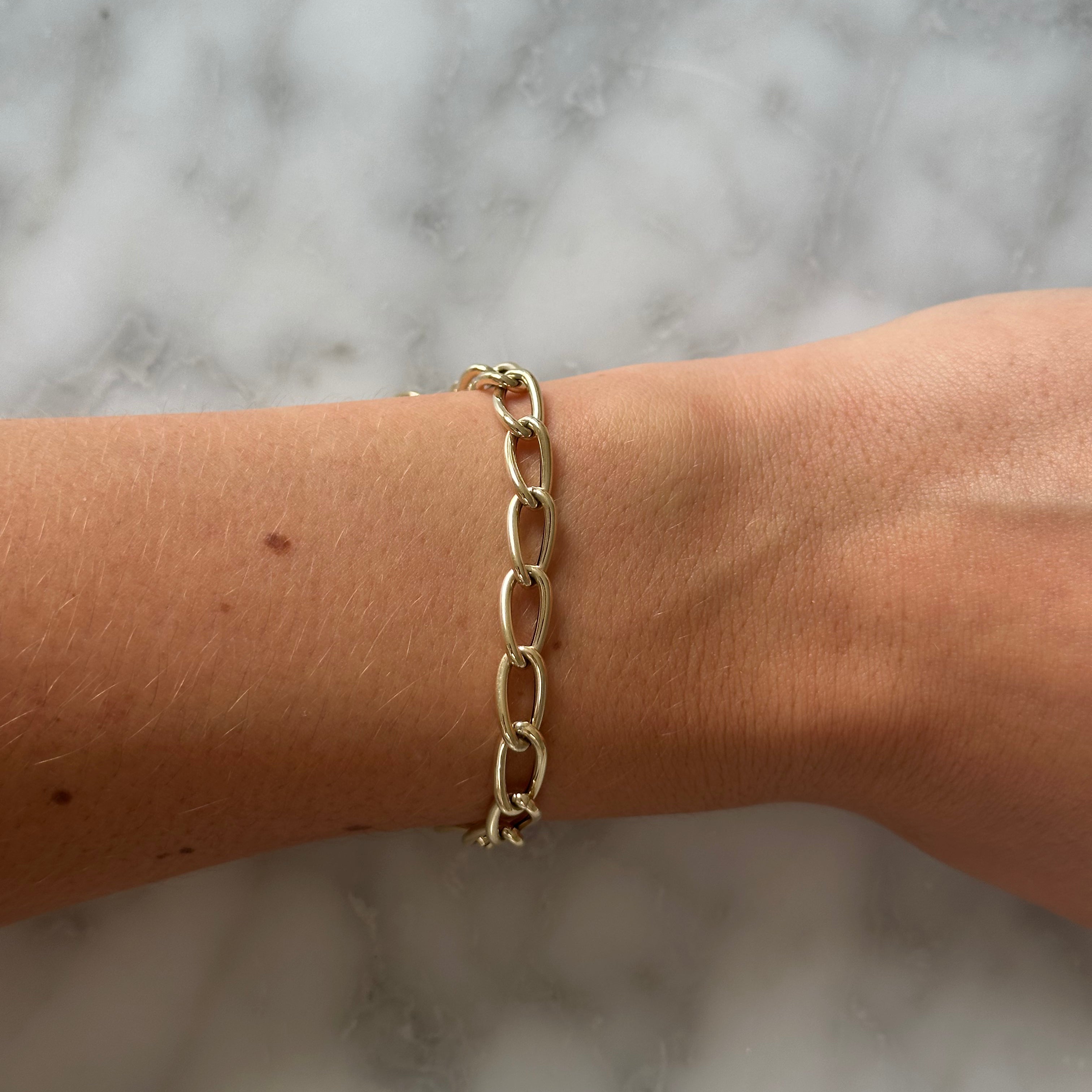 Gold chain bracelet on a wrist against a marble background