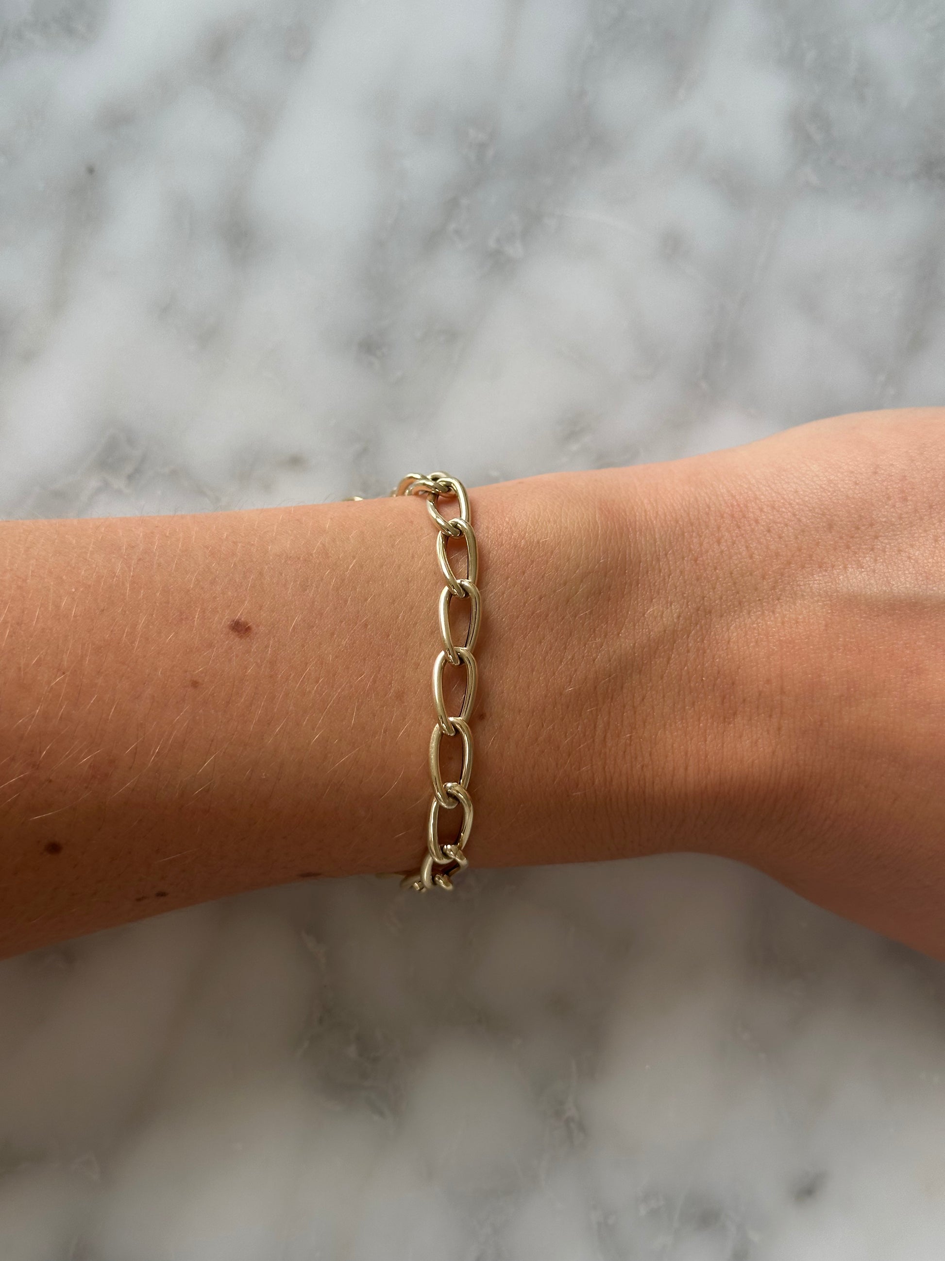 Gold chain bracelet on a wrist against a marble background