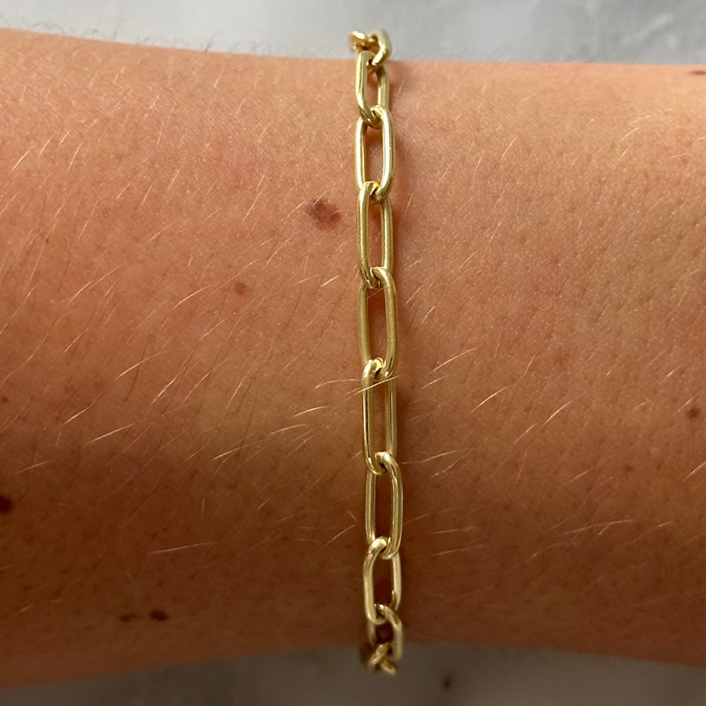 Gold chain bracelet on a wrist against a marble background