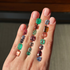 Hand wearing multiple gemstone rings with a neutral background