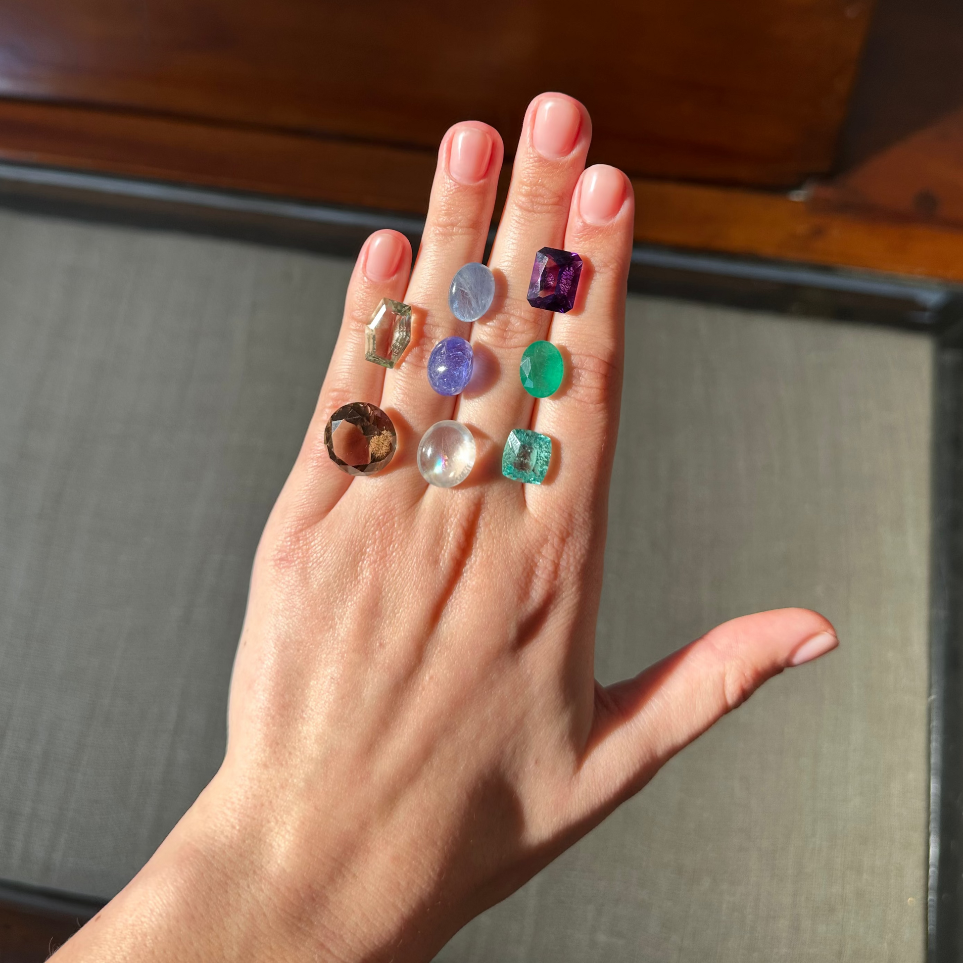 Hand holding multiple gemstones of various colors against a neutral background