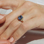 Gold ring with a blue gemstone on a hand against a white background