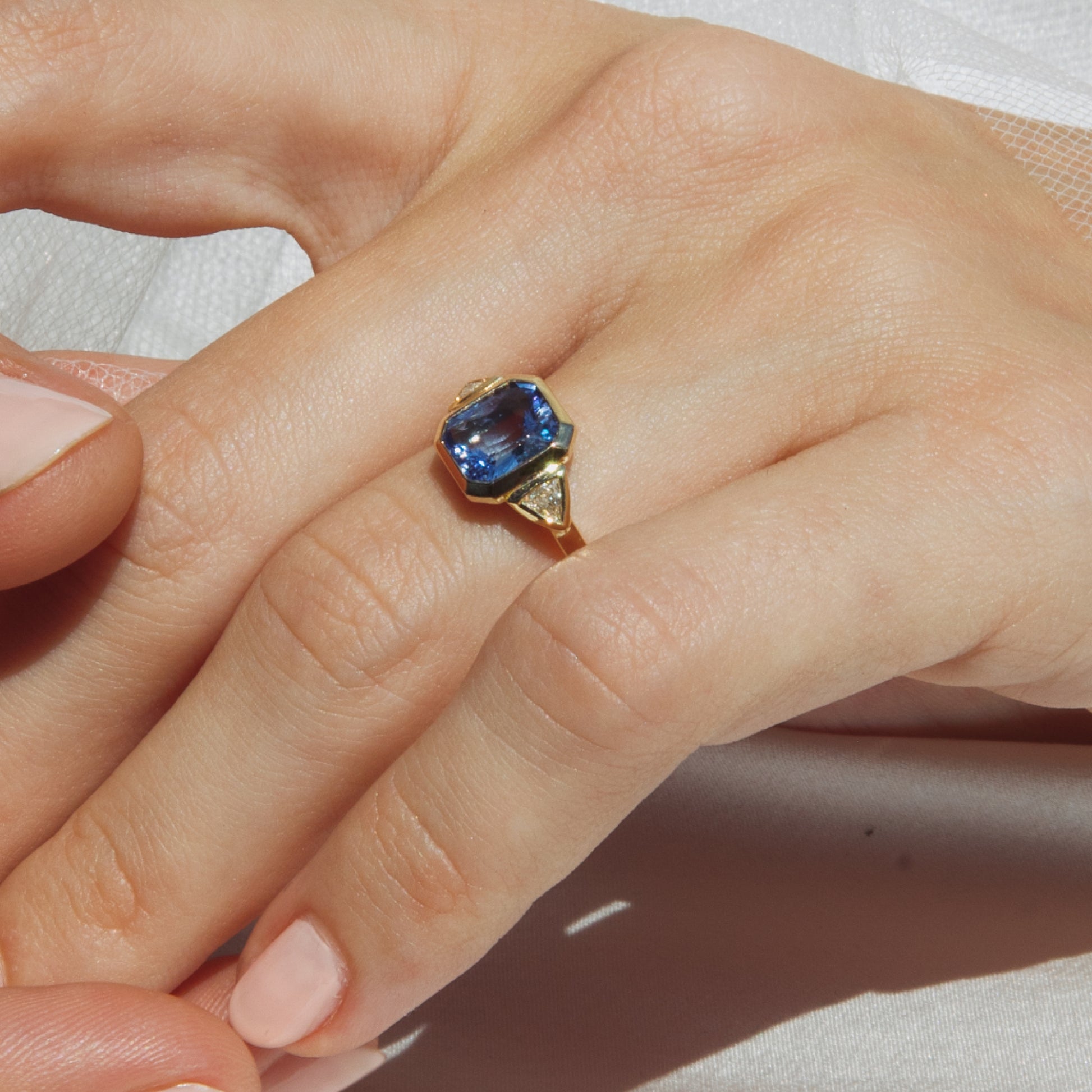Gold ring with a blue gemstone on a hand against a white background