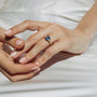 Close-up of a hand wearing a ring with a blue gemstone on a white fabric background