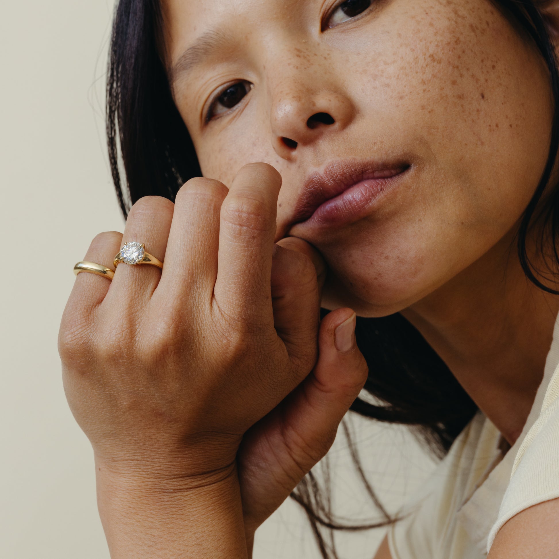 Close-up of a woman with a gold ring on her finger against a neutral background