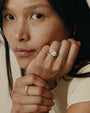Close-up of a person wearing two gold rings with a diamond on a neutral background