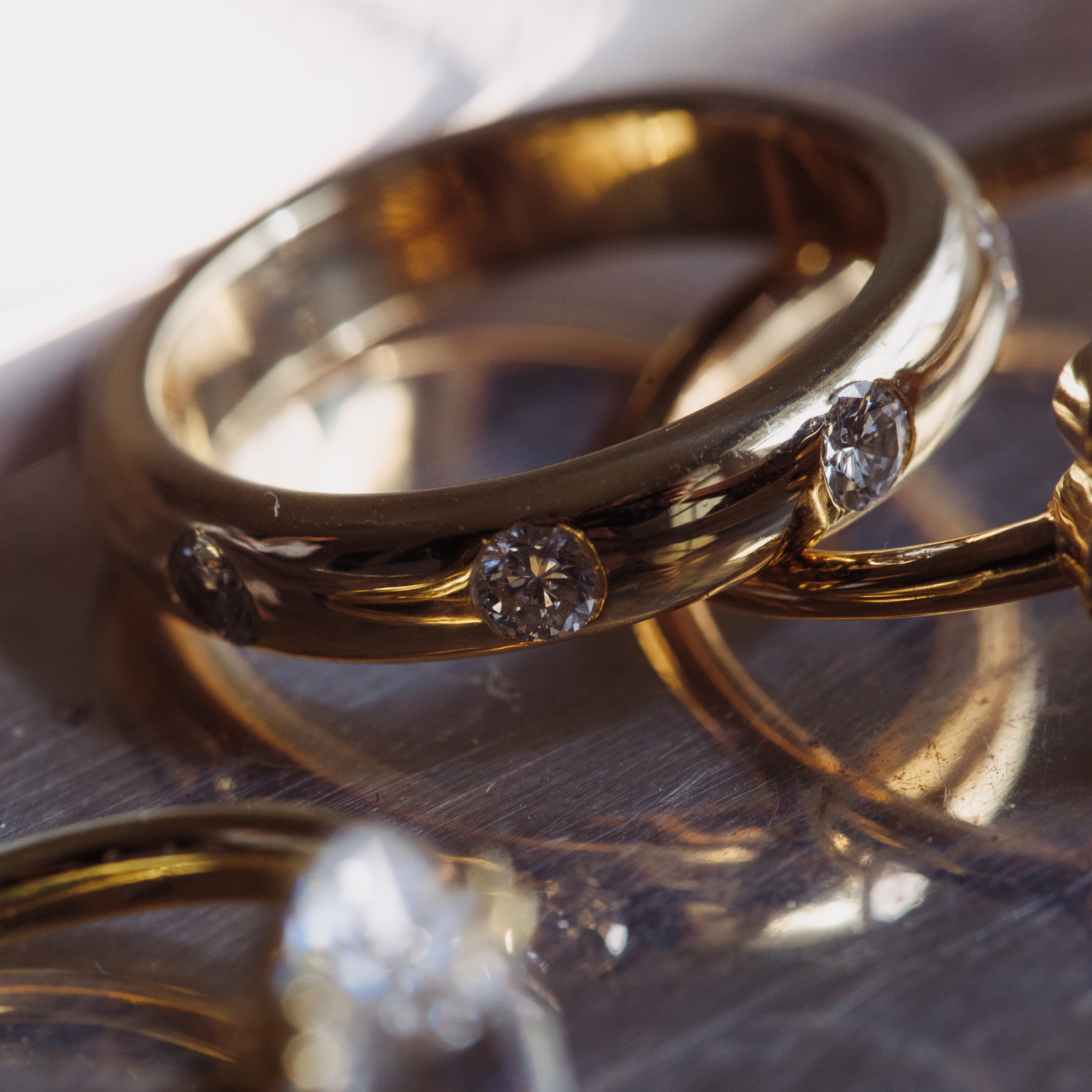 Close-up of two gold rings with diamond accents on a reflective surface.