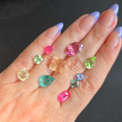 Hand holding various small colored gemstones against a dark background