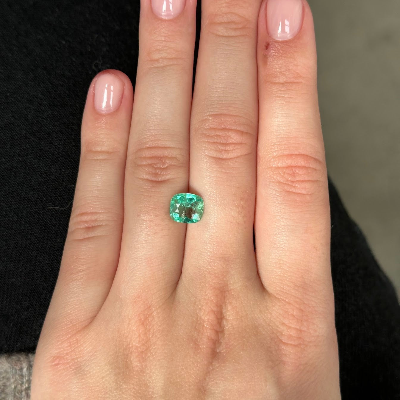 Hand holding a green emerald gemstone against a neutral background