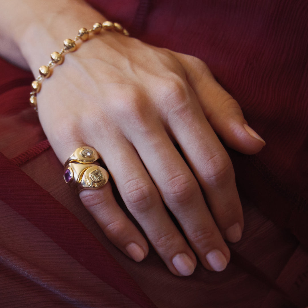 Hand wearing a gold ring and bracelet on a red fabric background