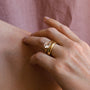 Close-up of a hand wearing two gold rings with a diamond on a pink fabric background