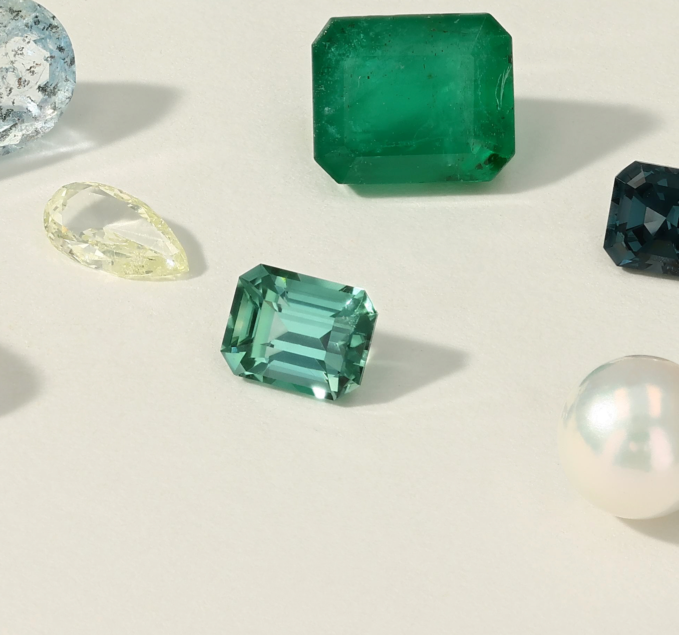 Collection of green gemstones and a pearl on a light background