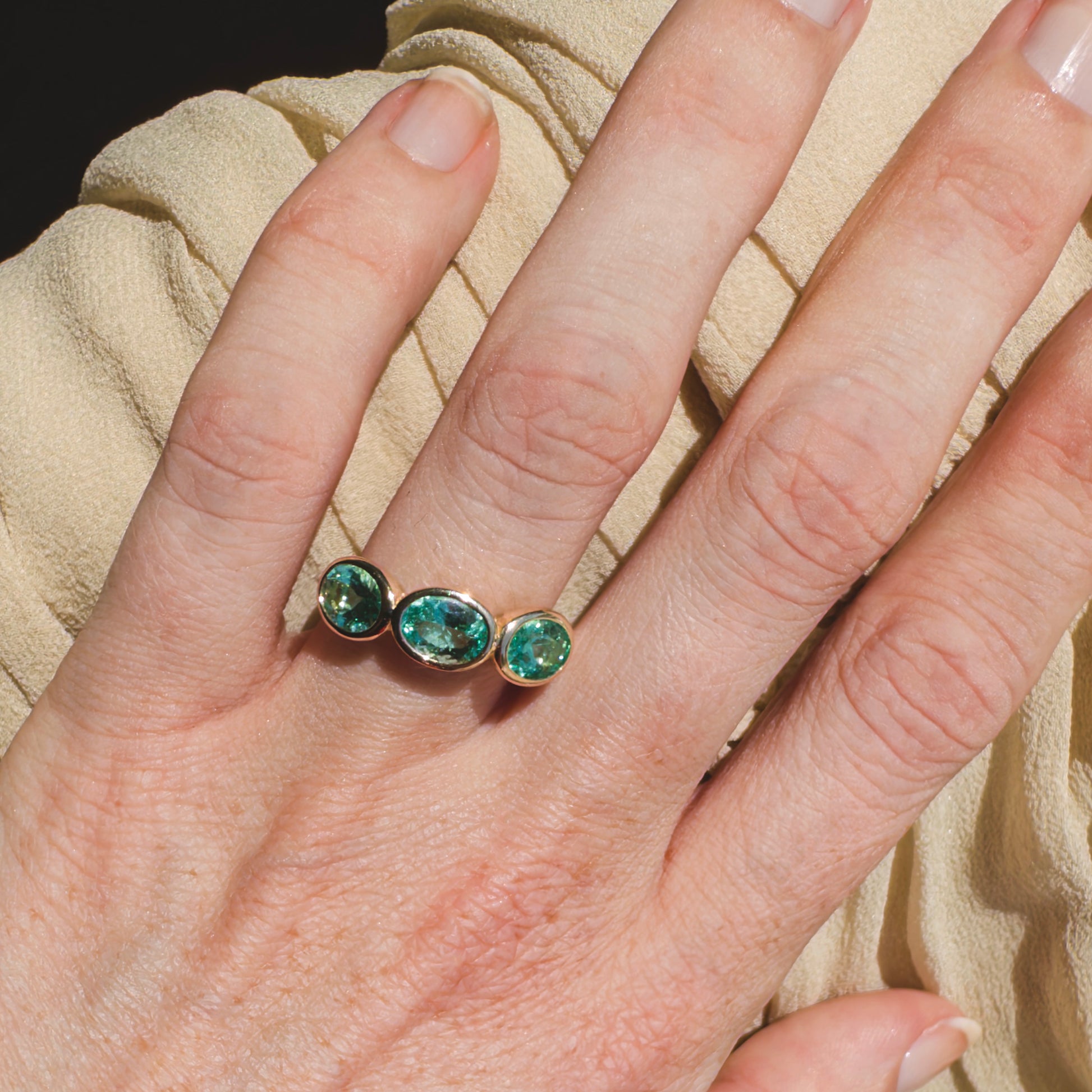 Ring with three green gemstones on a hand against a beige fabric background
