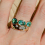 Gold ring with green gemstones on a hand against a beige background